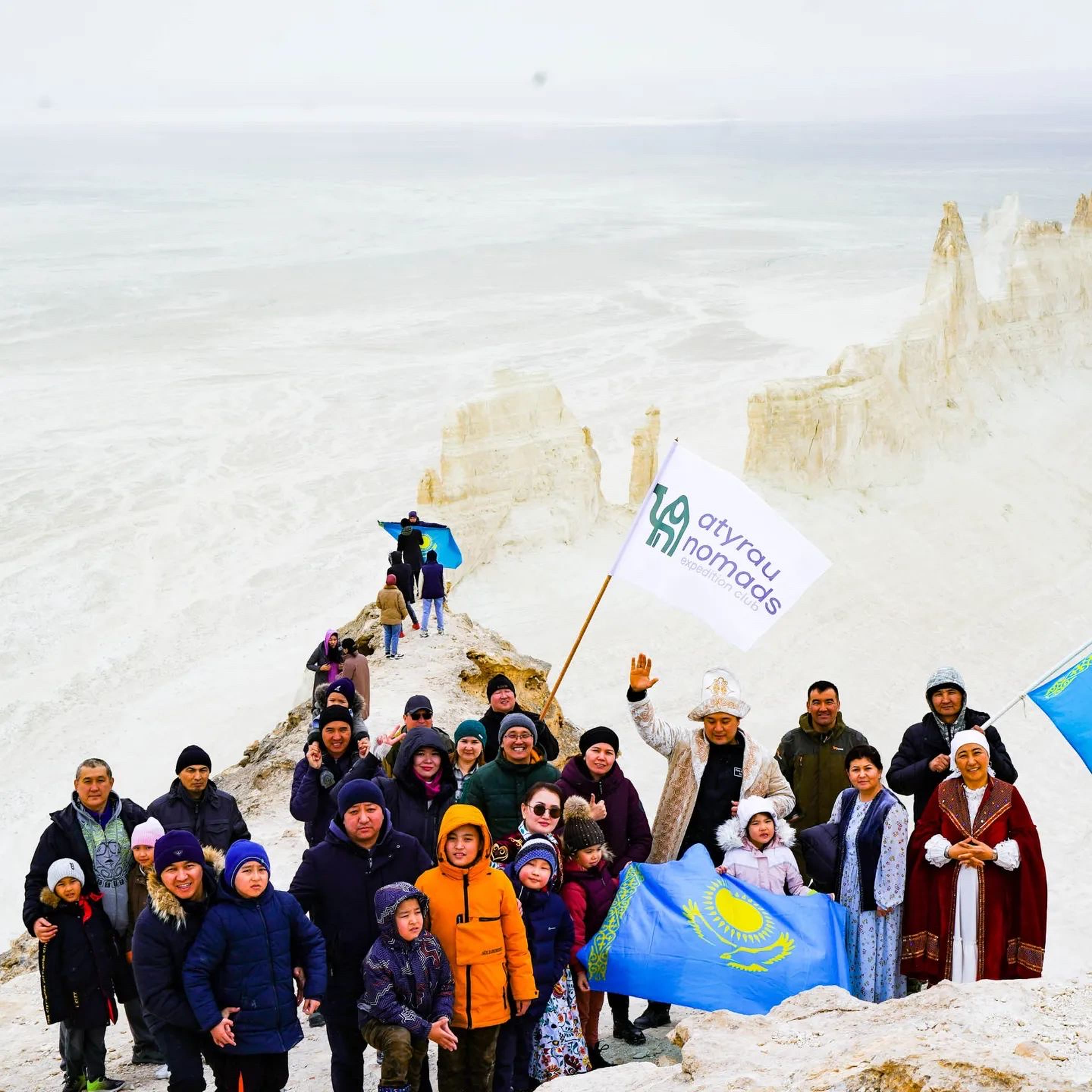 Участники и внедорожники Atyrau Nomads рядом с большим флагом Казахстана на Бозжыре